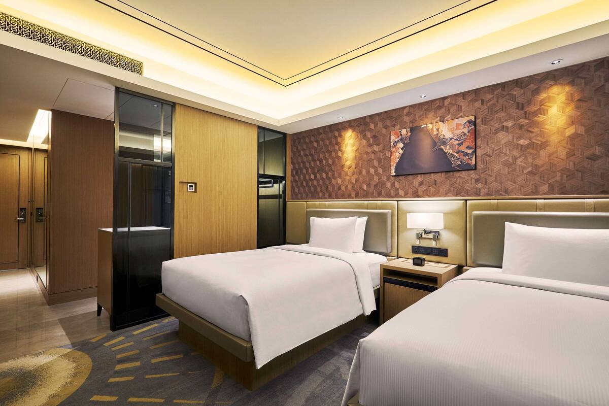 A hotel room with two beds, a wardrobe, a desk, and a wall-mounted artwork.