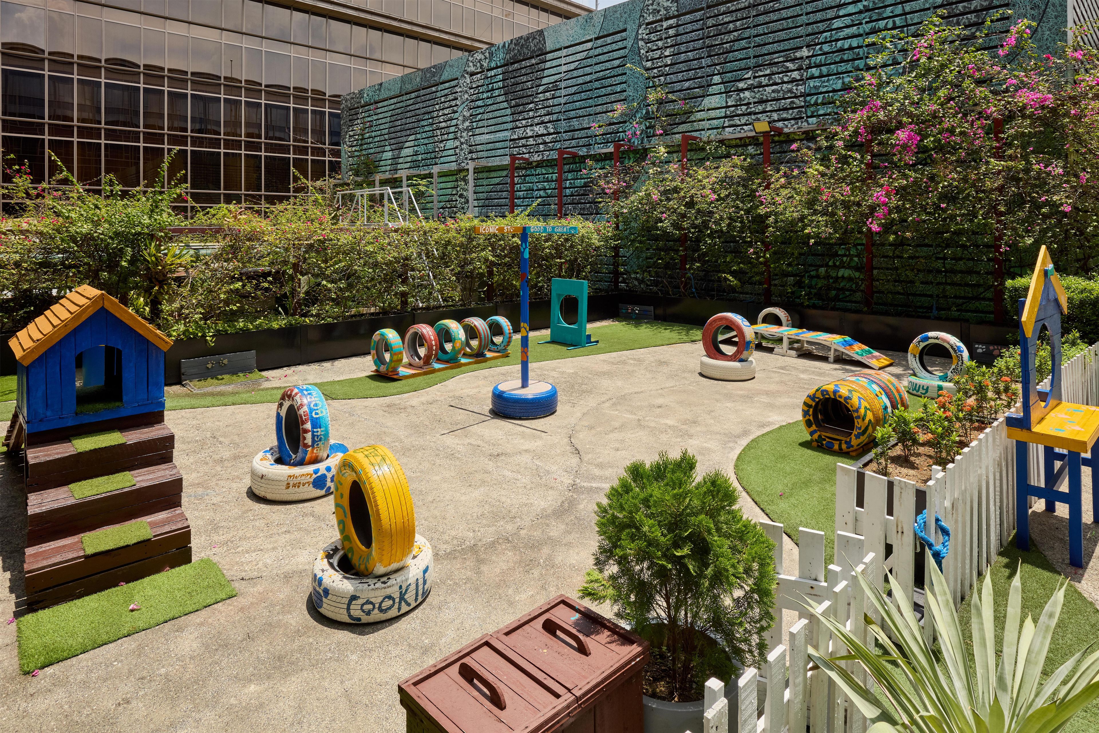 A playground with tire swings, a small blue house, and a white picket fence.