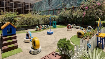 A playground with tire swings, a small blue house, and a white picket fence.
