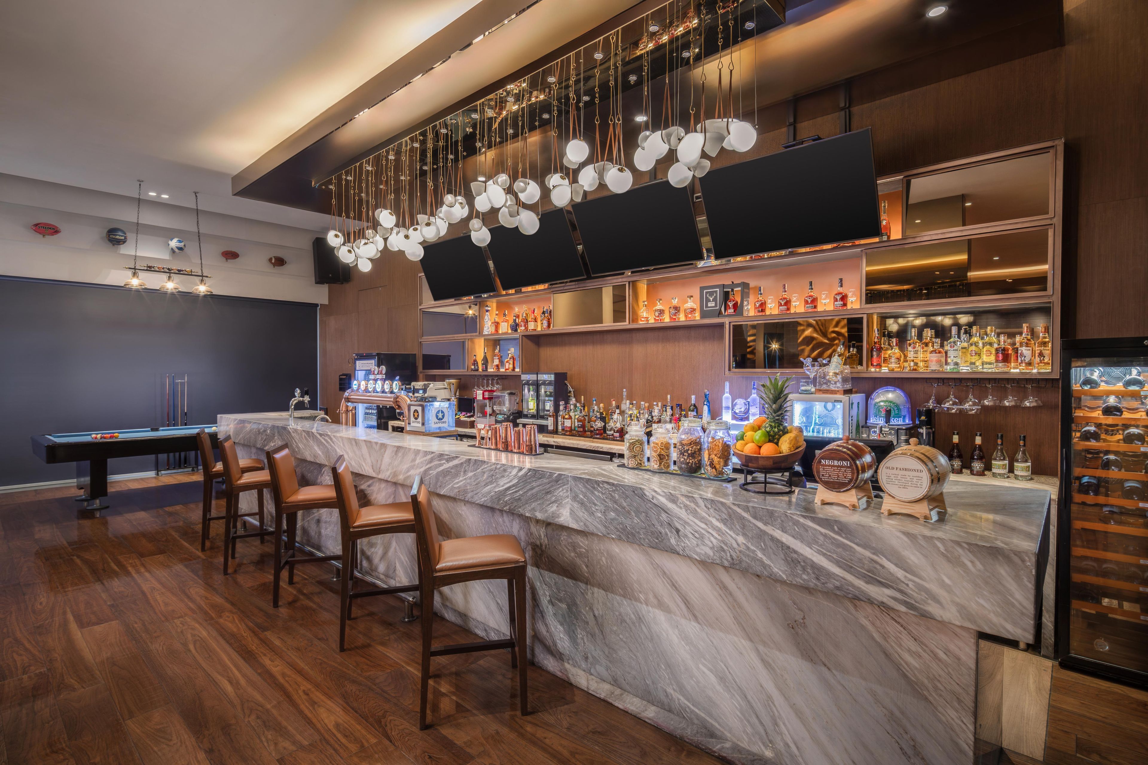 Un espace bar doté d’un comptoir en marbre, de nombreuses bouteilles d’alcool et d’une table de billard.