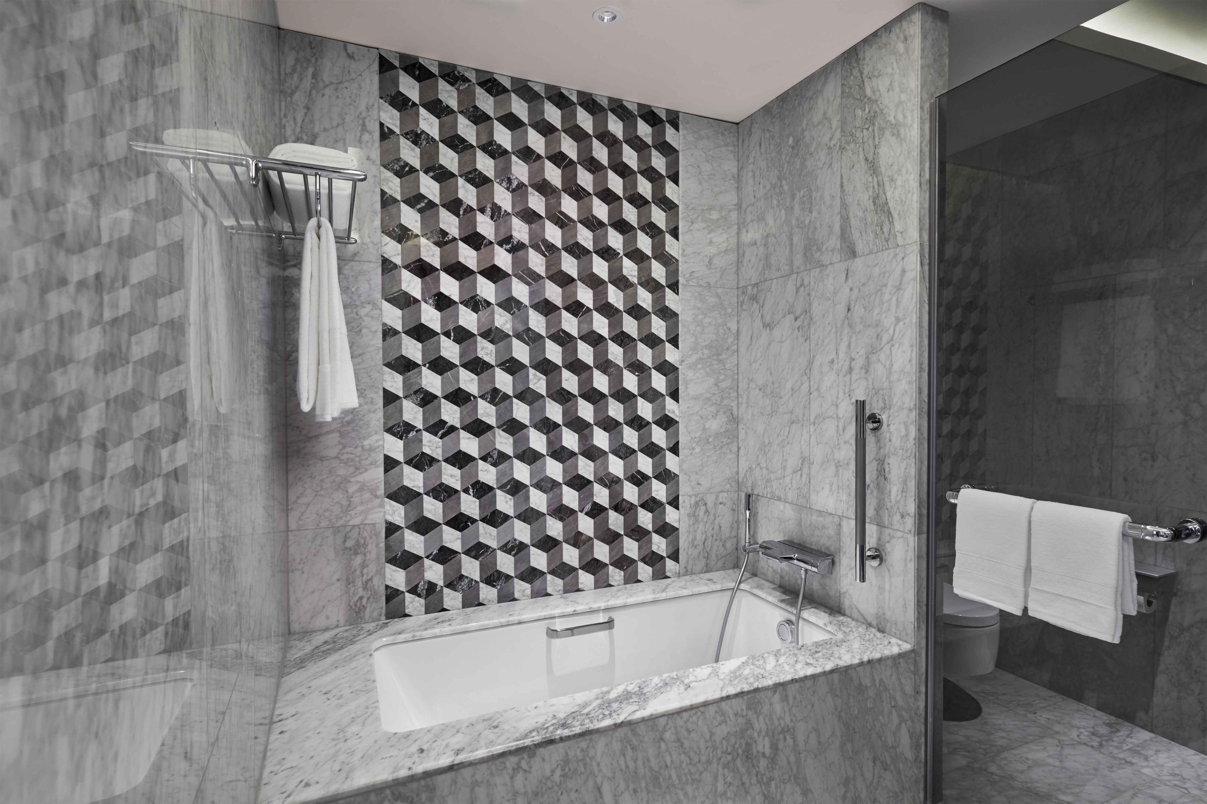 A modern bathroom with a geometric patterned wall, a freestanding bathtub, and a glass-enclosed shower area.