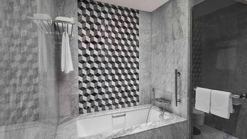 A modern bathroom with a geometric patterned wall, a freestanding bathtub, and a glass-enclosed shower area.