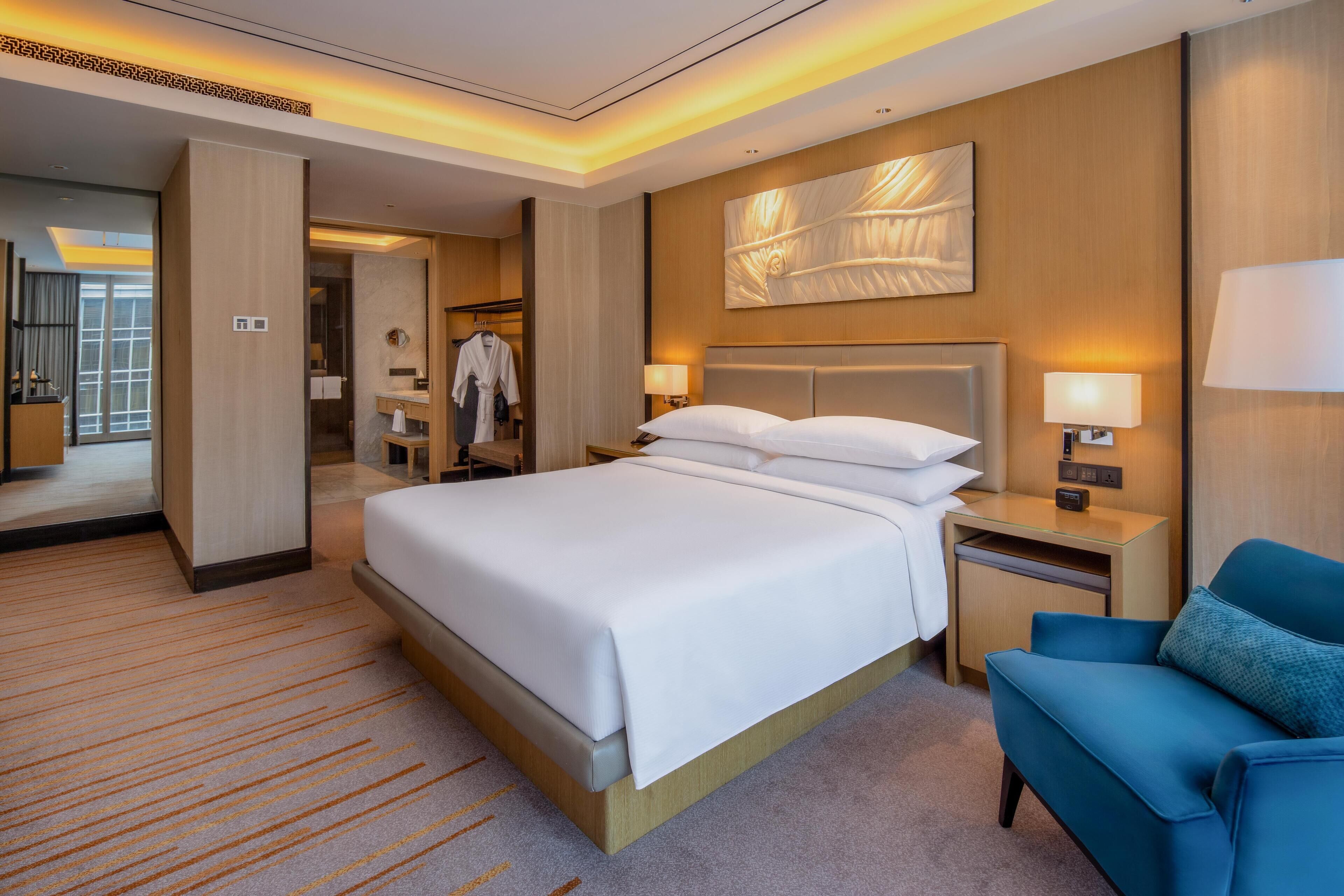 A hotel room with a large bed, bedside tables, a desk, a chair, and a large mirror.
