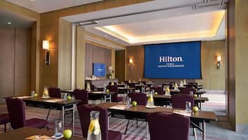 Une salle de conférence à l’hôtel Hilton de Manille, équipée de tables, de chaises et d’un grand écran affichant le nom de l’hôtel.