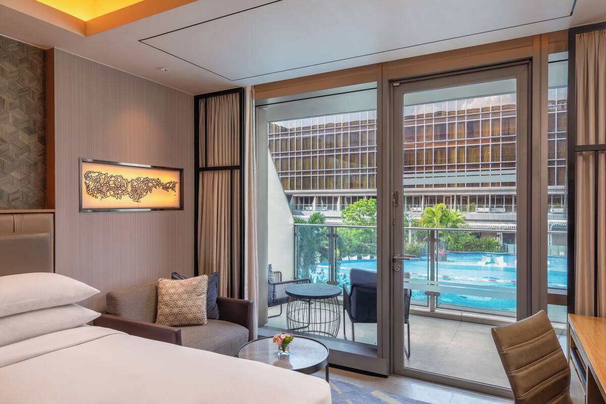 A hotel room with a large sliding glass door leading to a balcony with a pool view.