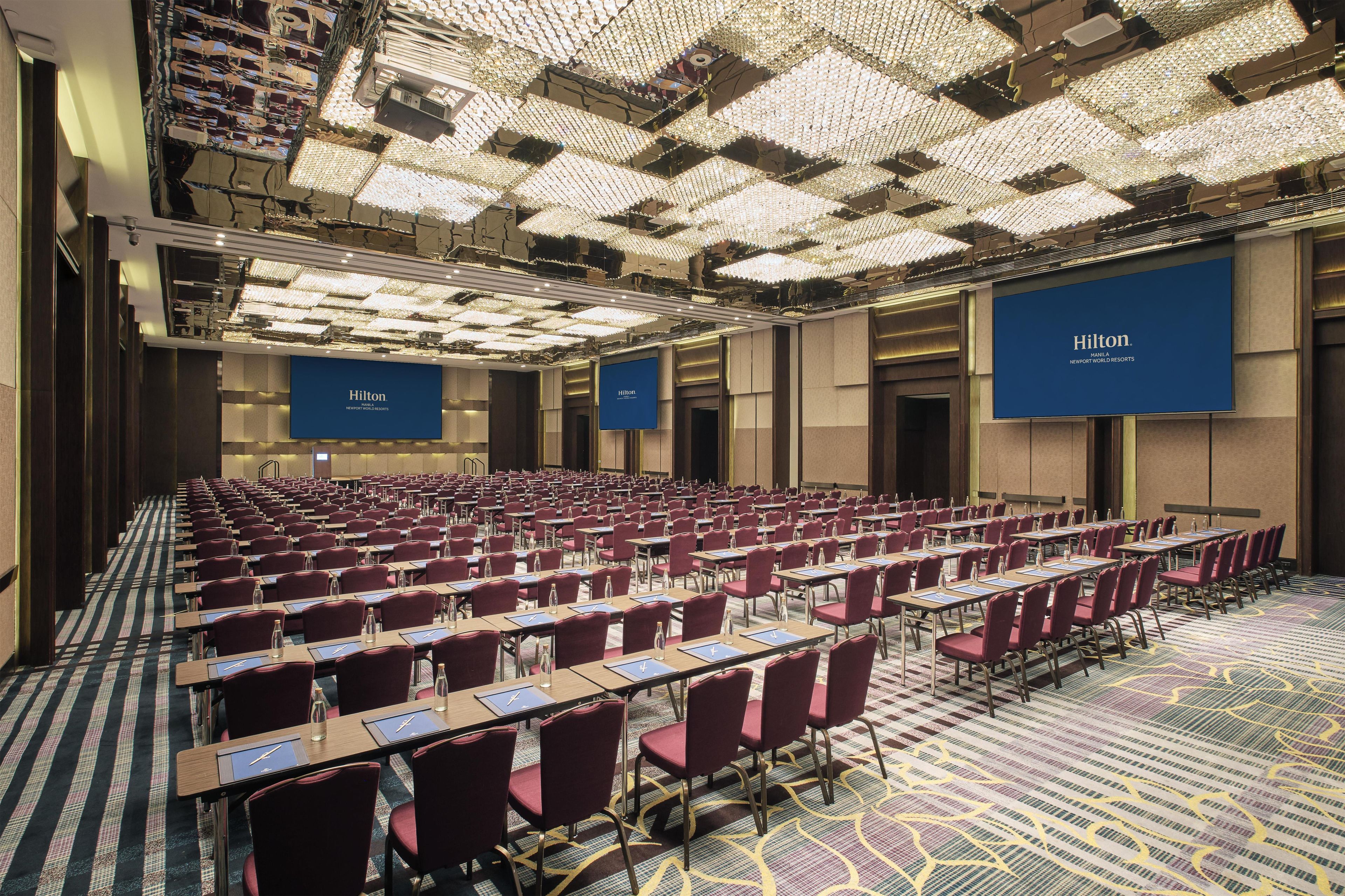 A large conference room with rows of tables and chairs, blue signage, and a patterned carpet.