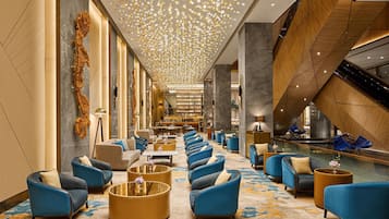 A hotel lobby with a long reception desk, seating area with sofas and armchairs, and a decorative ceiling.