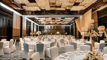 A banquet hall with round tables, white chairs, and chandeliers.