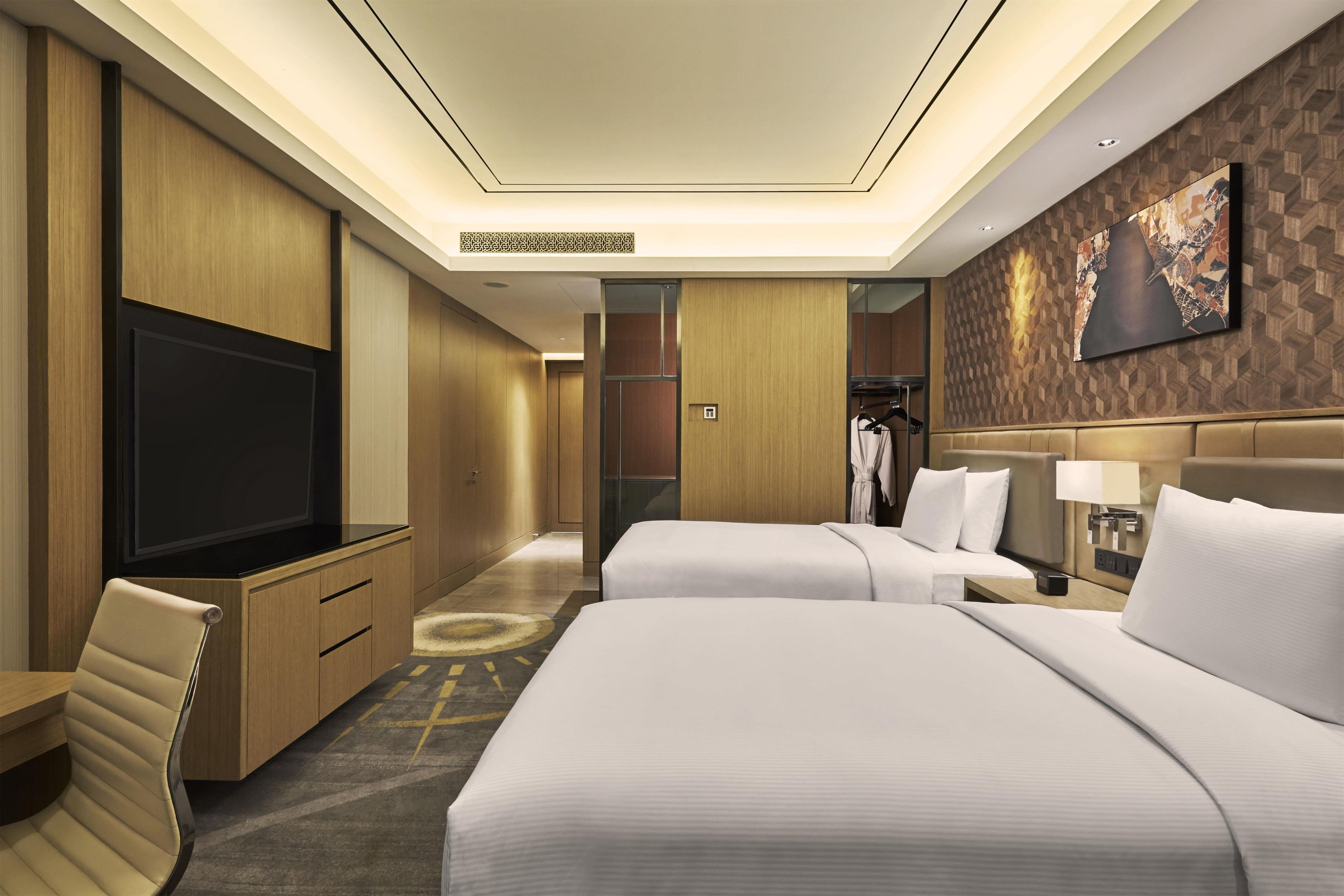 A hotel room with two beds, a TV, a wardrobe, and a mirror.