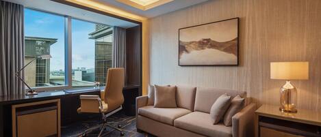 Una habitación de hotel con un ventanal grande, un sofá, un escritorio y una lámpara.