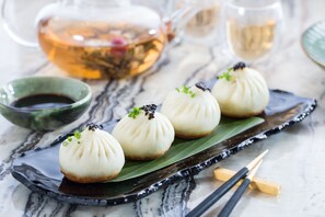 A table with four steamed buns on a leaf, a teapot, and a cup of tea. - Hilton Manila Newport World Resorts (Pasay)