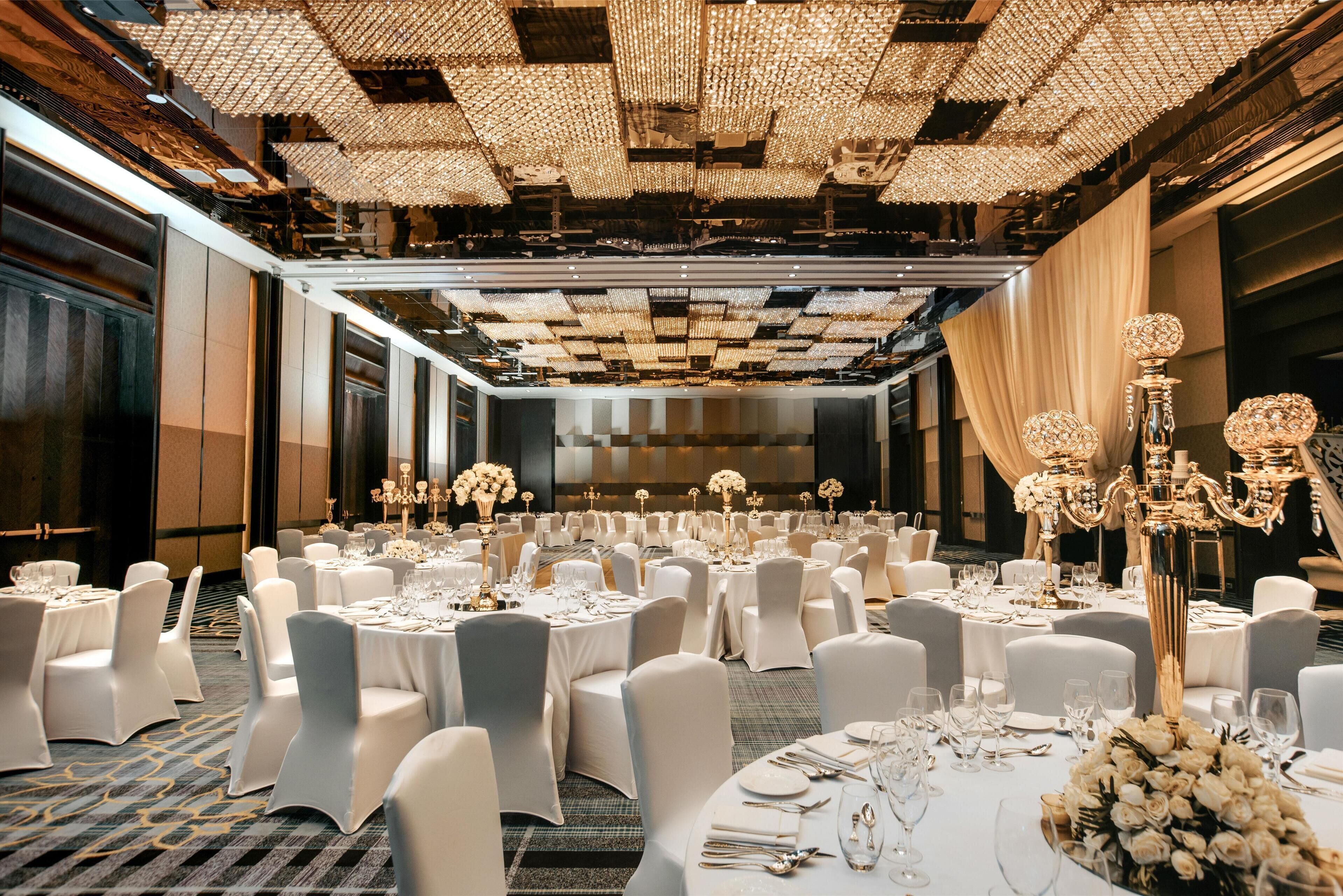 Un salón de banquetes con mesas redondas dispuestas para comer, sillas blancas y candelabros.