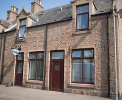 A two-story stone building with a traditional design, featuring a set of double doors and windows with curtains.
