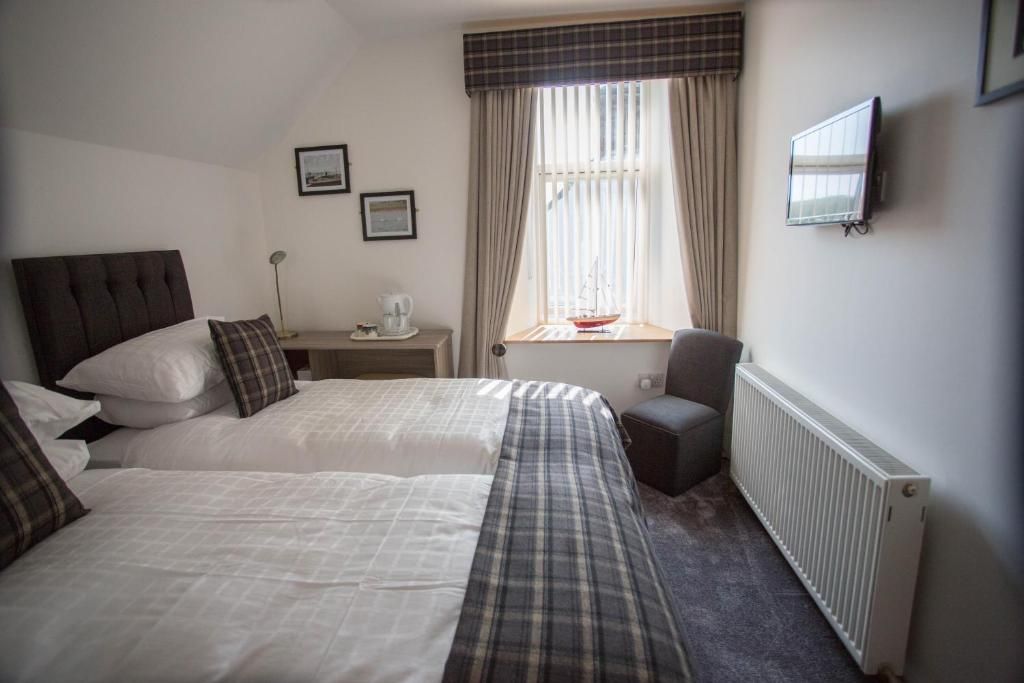 A bedroom with two beds, a desk with a chair, a radiator, and a window with curtains.
