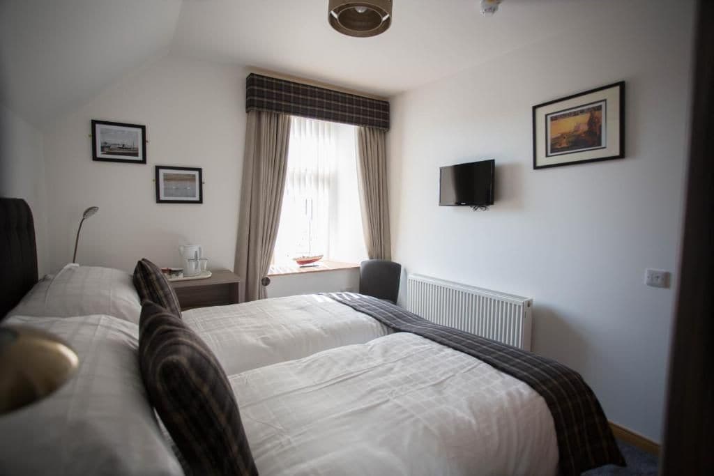 A hotel room with two beds, a flat-screen TV, a window with curtains, and framed pictures on the wall.