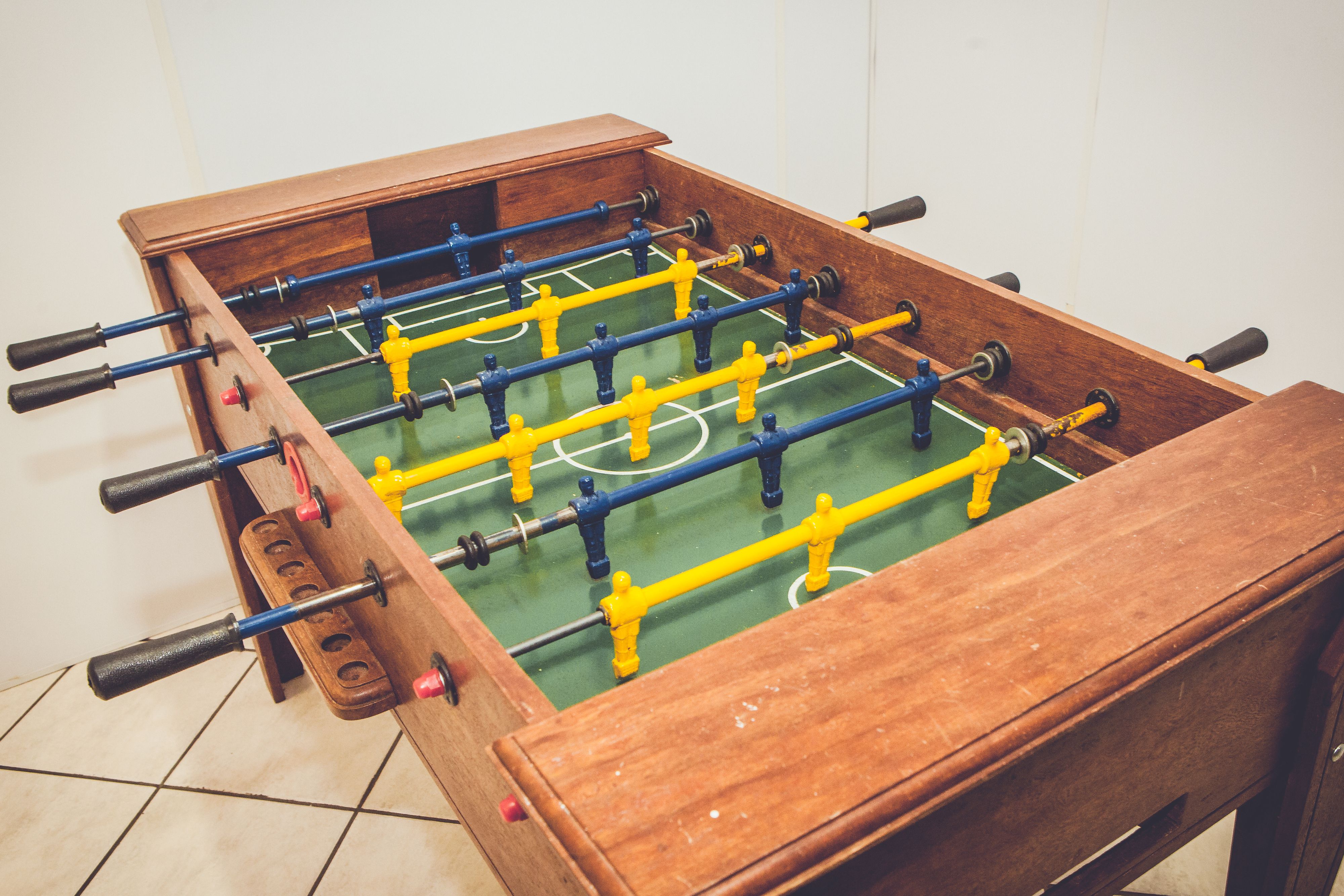 A wooden foosball table with a green playing surface and yellow and blue player figures.