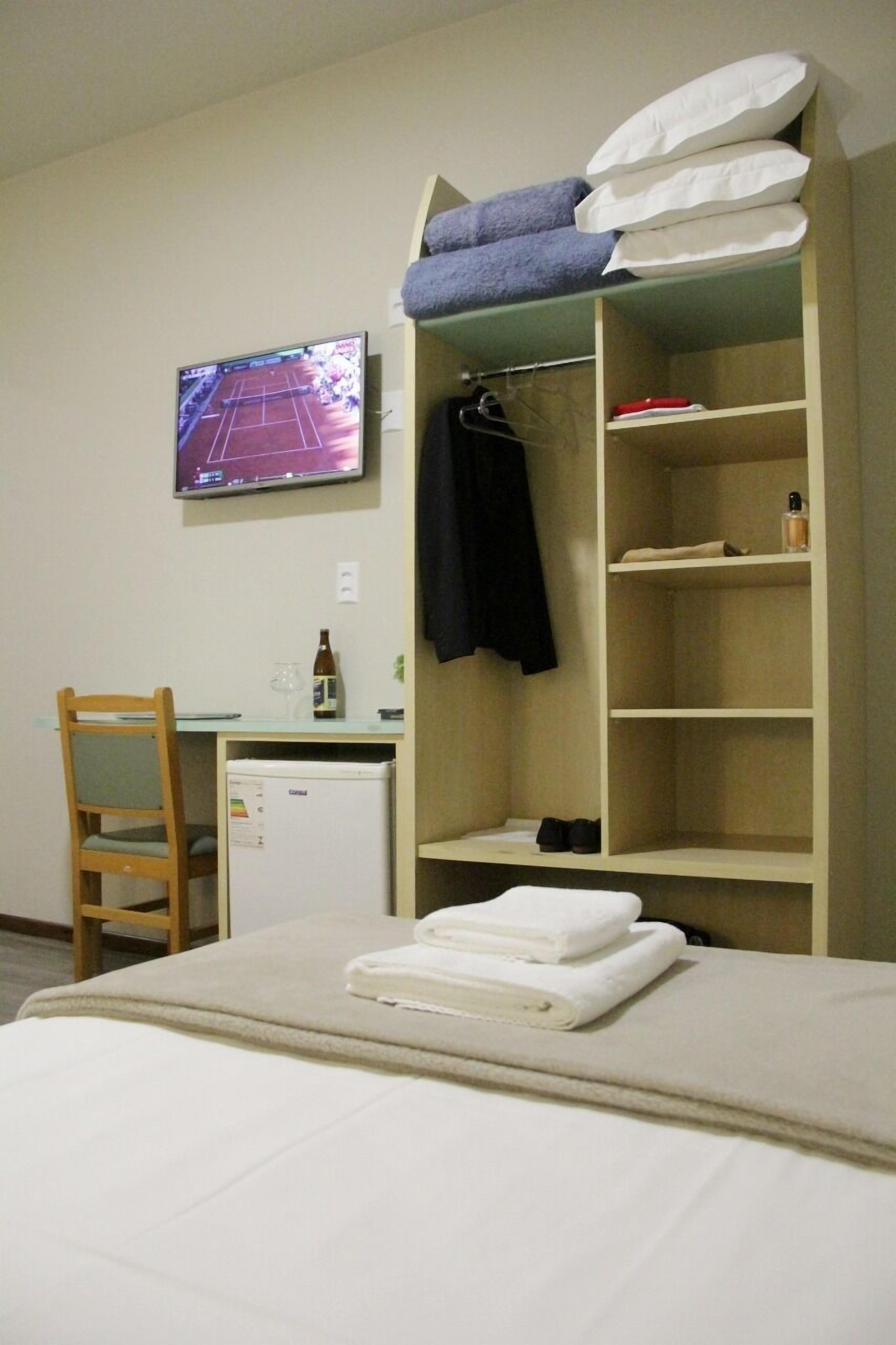 Ein Schlafzimmer mit einem Bett, einem Schreibtisch mit Computer, einem Fernseher und einem Kleiderschrank.