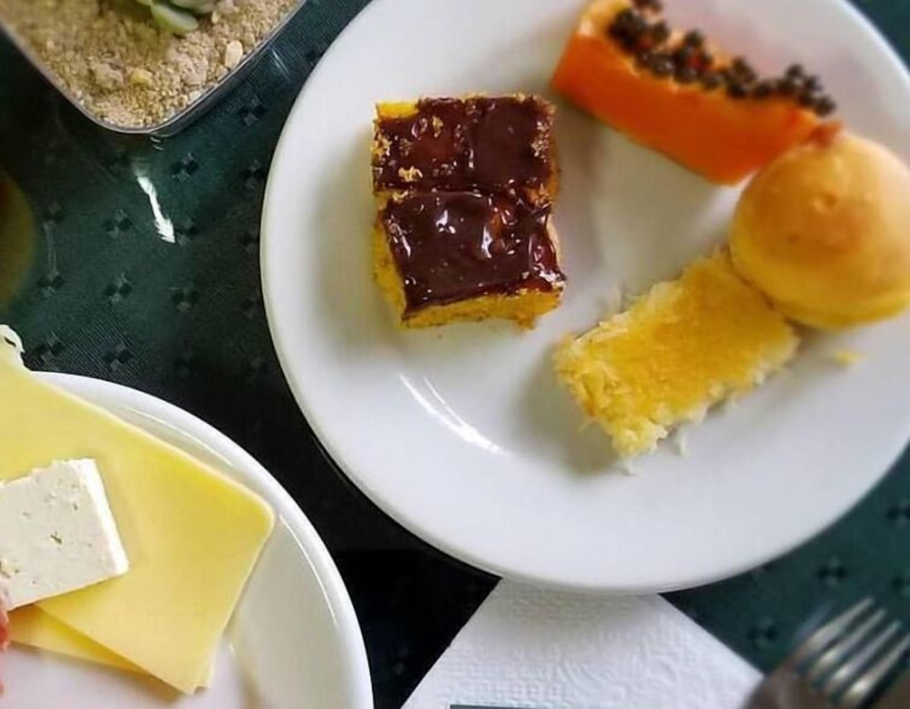 Um prato com um pedaço de bolo de chocolate, uma fatia de pão e uma laranja pequena.