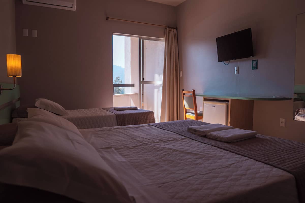 A hotel room with two beds, a television, a desk, and a window with curtains.