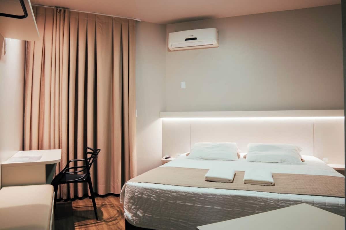 A hotel room with a bed, a desk, a chair, and a window with curtains.