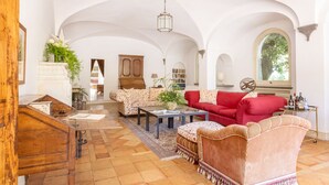 A spacious living room with high ceilings, a red sofa, a patterned armchair, and a wooden cabinet. - Villa Gallone (Sorrento)