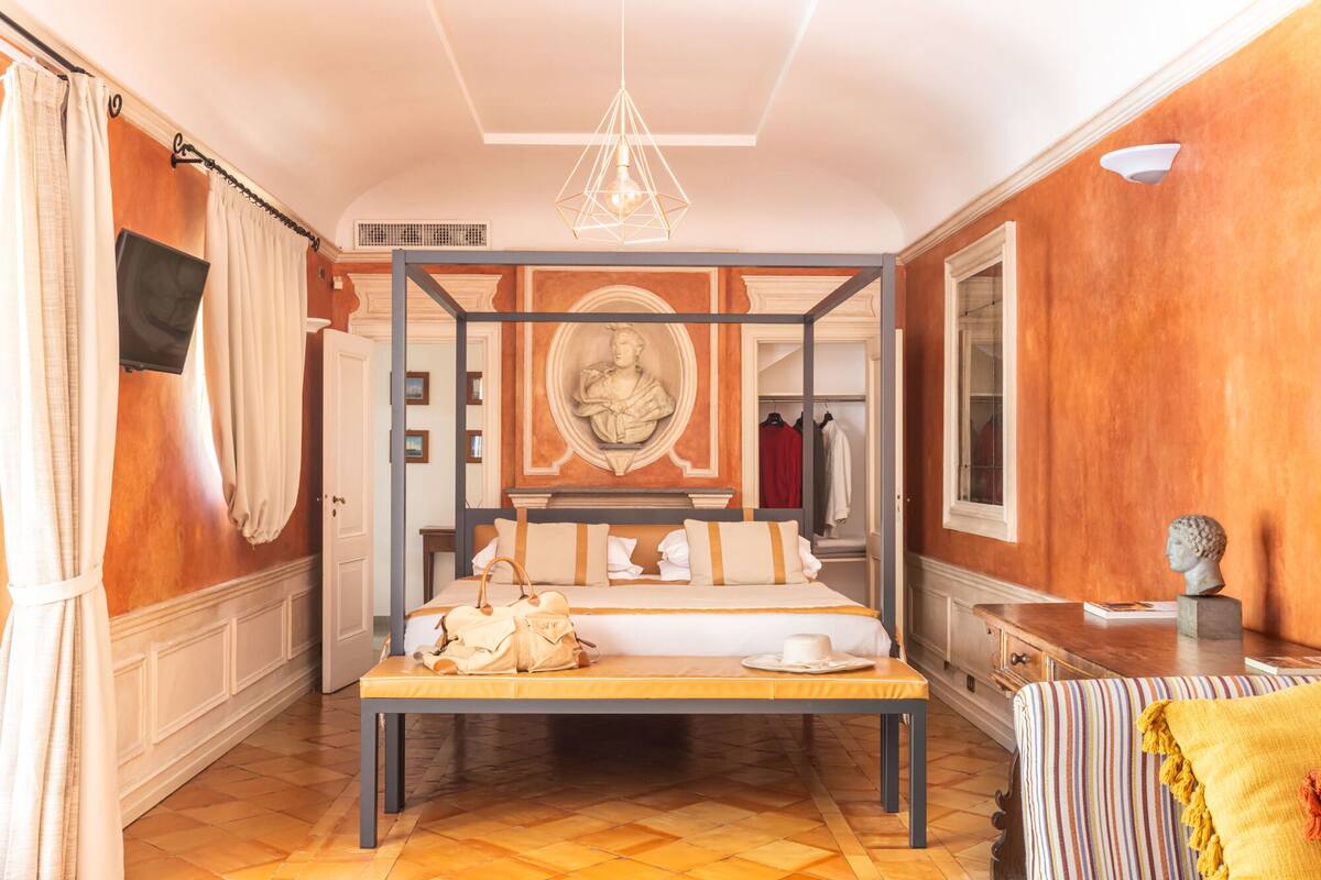 A four-poster bed with a wooden frame, a bench at the foot of the bed, and a mirror above the bed.