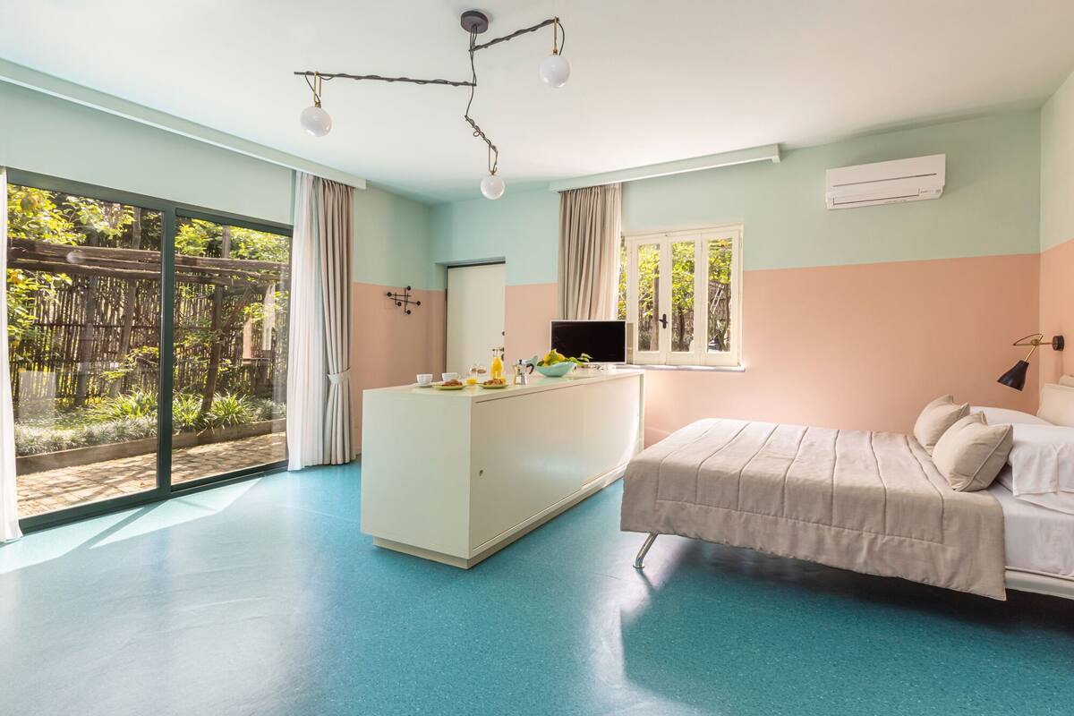 A bedroom with a bed, a desk with a TV, and a large window.
