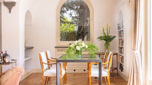 A dining area with a glass table, white chairs, a vase with flowers, and a bookshelf. - Villa Gallone (Sorrento)