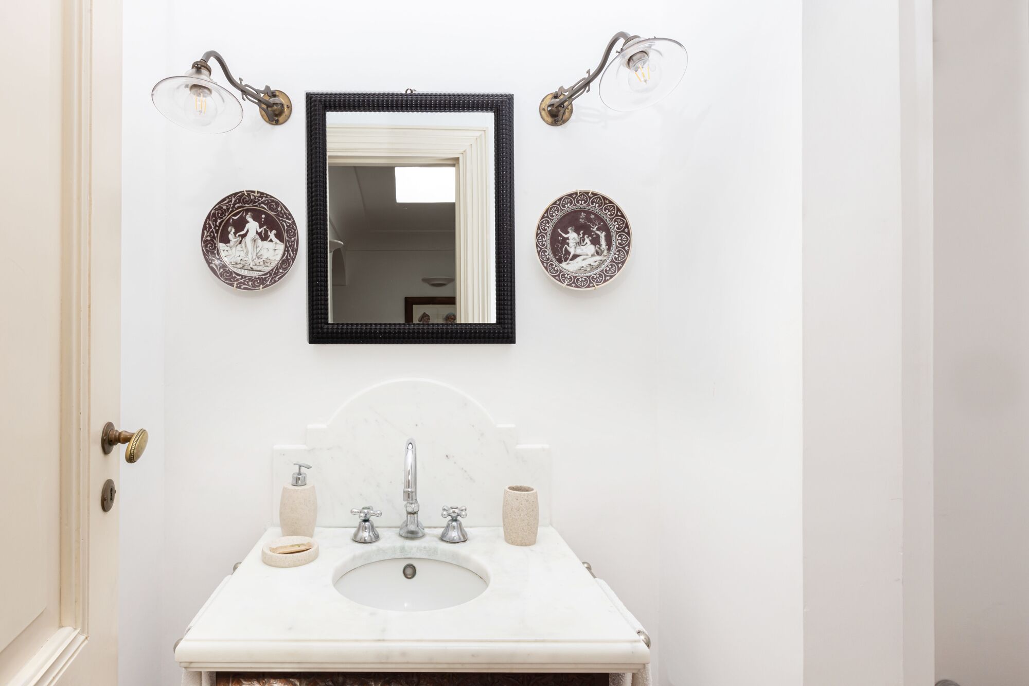Ein Badezimmer mit einem weißen Waschbecken, zwei Wandleuchten, einem Spiegel und zwei Dekotellern.