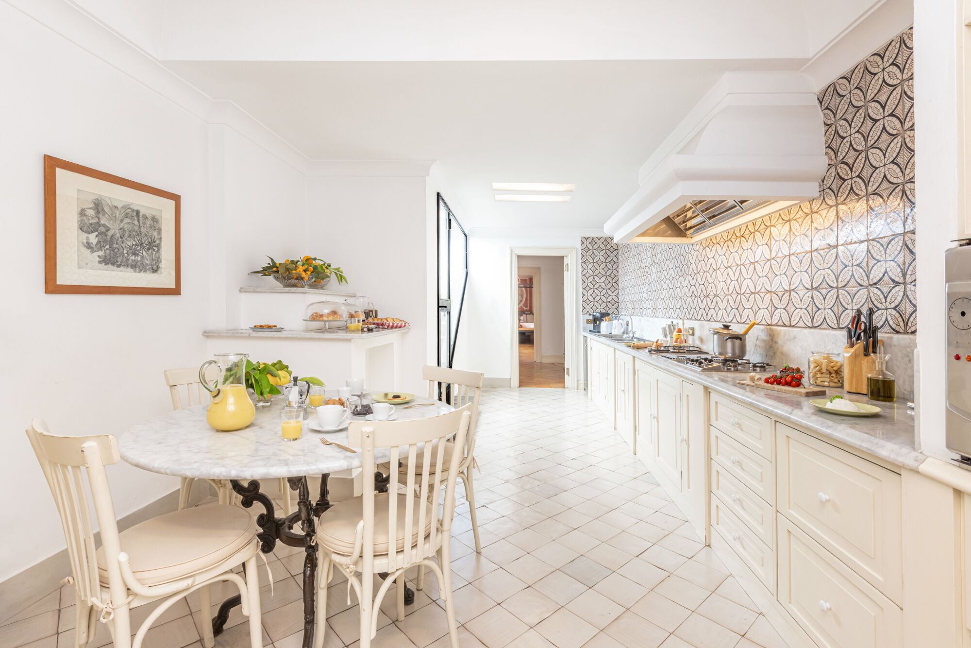 A bright kitchen with white cabinets, a marble countertop, and a patterned backsplash.
