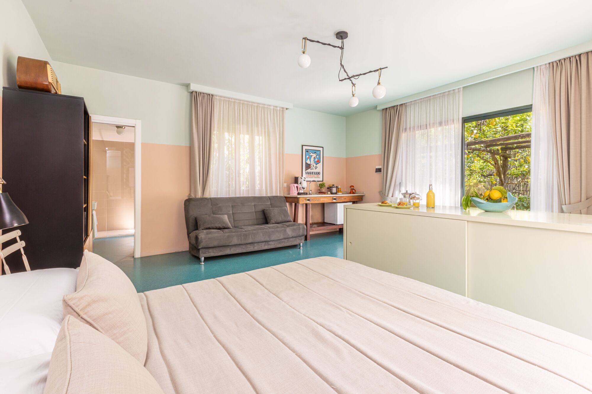 Quarto com cama, sofá, escrivaninha e janela com cortinas.