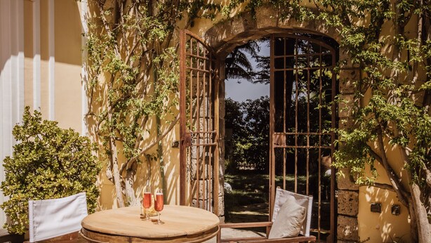 An outdoor patio with a round wooden table and four chairs, surrounded by lush greenery and a stone wall. - Villa Gallone (Sorrento)