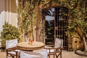 An outdoor patio with a round wooden table and four chairs, surrounded by lush greenery and a stone wall. - Villa Gallone (Sorrento)