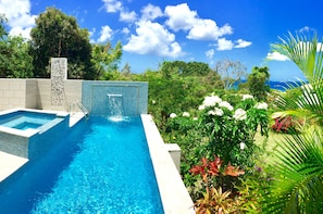 Une piscine dotée d’un bassin aux eaux d’un bleu limpide, entourée d’une végétation luxuriante et offrant une vue sur l’océan.