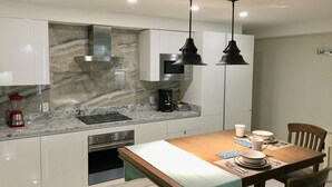 A modern kitchen with white cabinets, a marble backsplash, a built-in oven, and a dining area with a wooden table set for four. - La Porta Della Casa (Prospect)