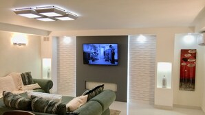 A modern living room with a flat-screen TV mounted on the wall, a green sofa with patterned cushions, and a decorative wall piece. - La Porta Della Casa (Prospect)
