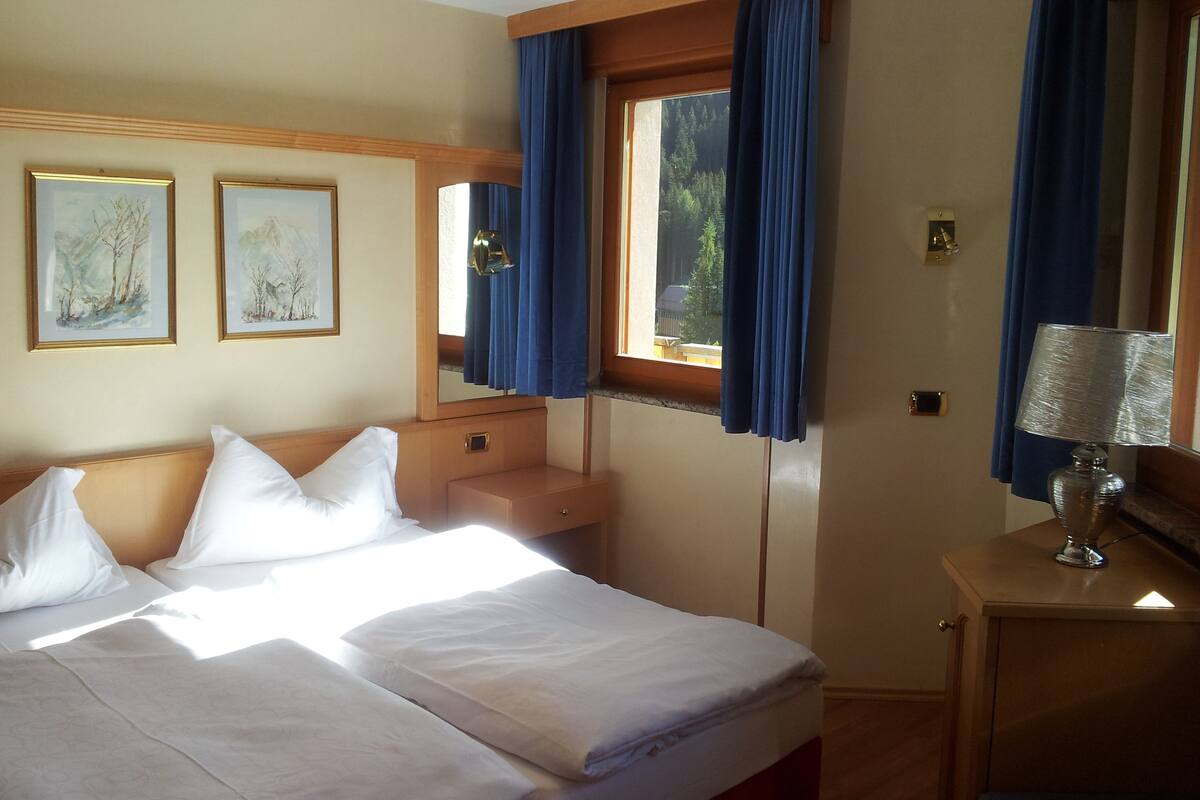 A hotel room with a bed, a bedside table, a lamp, a mirror, and two framed pictures on the wall.