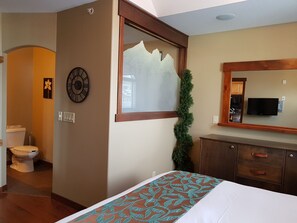 Un dormitorio con una cama, un aparador, un espejo, un reloj y una ventana con vistas al exterior.