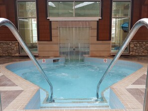 Una piscina con dos escaleras metálicas, un cartel que prohíbe los clavados y una pared de piedra.