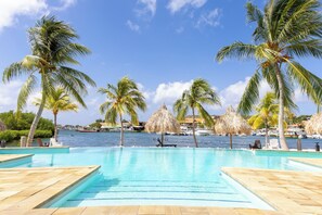 A clear blue pool with palm trees and a view of the sea.