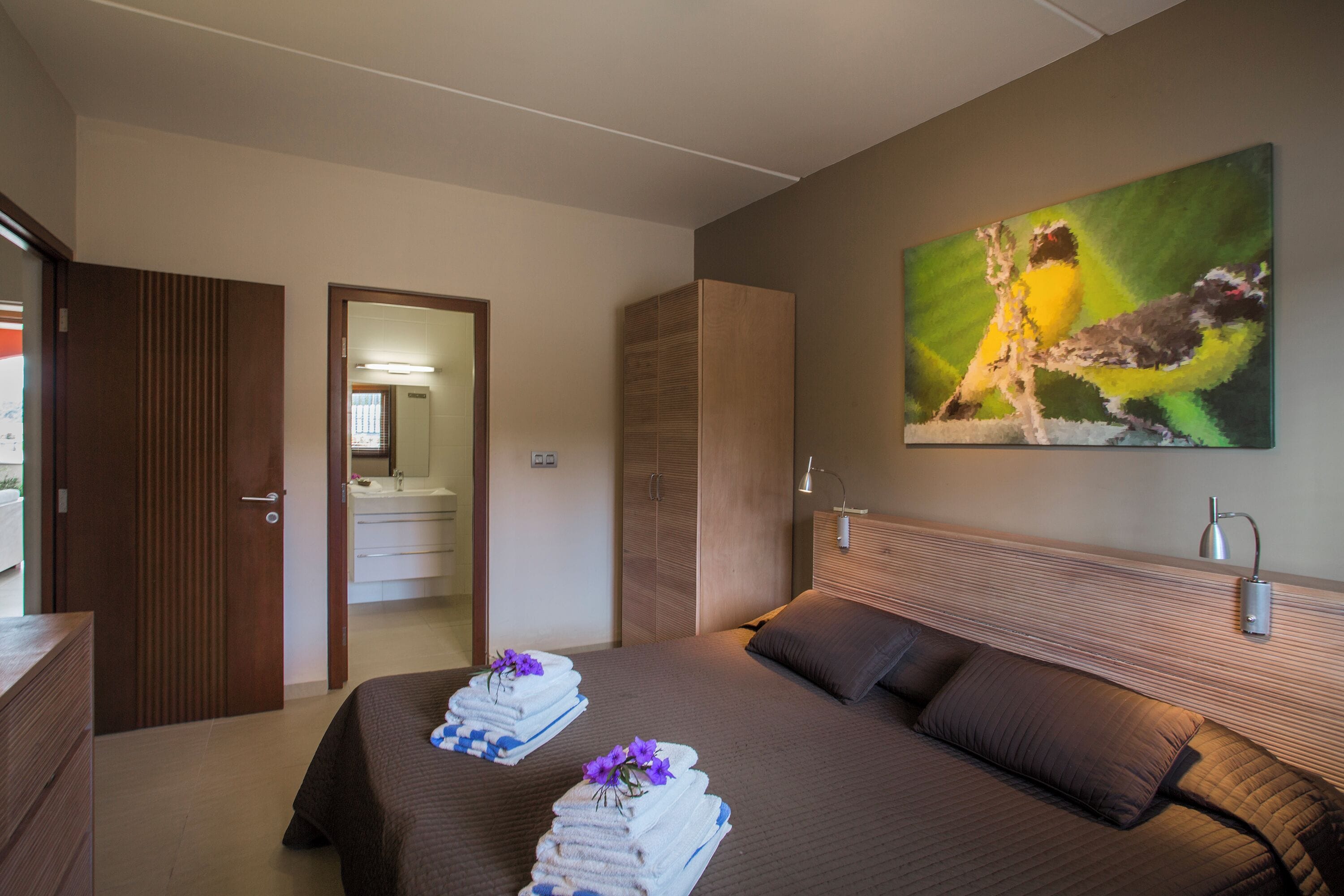 A hotel room with a bed, a bathroom, and a painting on the wall.