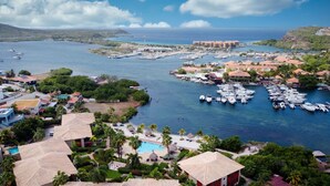A marina with numerous boats docked, surrounded by lush greenery and residential buildings. - Spanish Water Apartments (Jan Thiel)