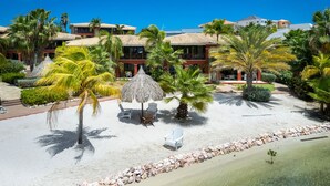 A resort with a sandy beach, palm trees, and a thatched umbrella. - Spanish Water Apartments (Jan Thiel)