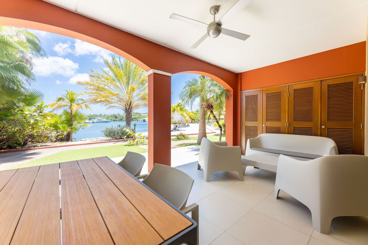 Un patio exterior con mesa y sillas de madera, un sofá blanco y armarios de madera.