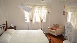 Un dormitorio con cama, una silla, un ventilador y una ventana con cortinas.