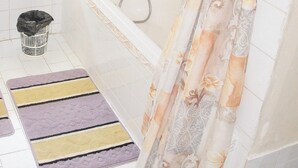 Un baño con bañera, ducha, ventana con persianas, un cesto de basura y una alfombra colorida.