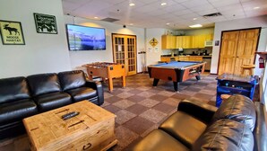 A living room with a pool table, a sofa, a coffee table, and a television. - Sunset Mountain Inn and Spa (Canmore)