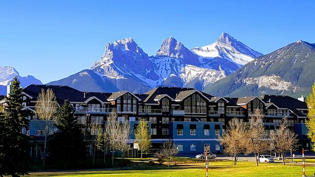 A hotel with a row of traditional European-style buildings, set against a backdrop of snow-capped mountains under a clear blue sky. - Sunset Mountain Inn and Spa (Canmore)