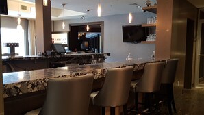 A bar area with a marble countertop, bar stools, pendant lighting, and a television mounted on the wall. - Sunset Mountain Inn and Spa (Canmore)