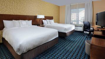 A hotel room with two beds, a desk with a computer, a TV, and a window with curtains.